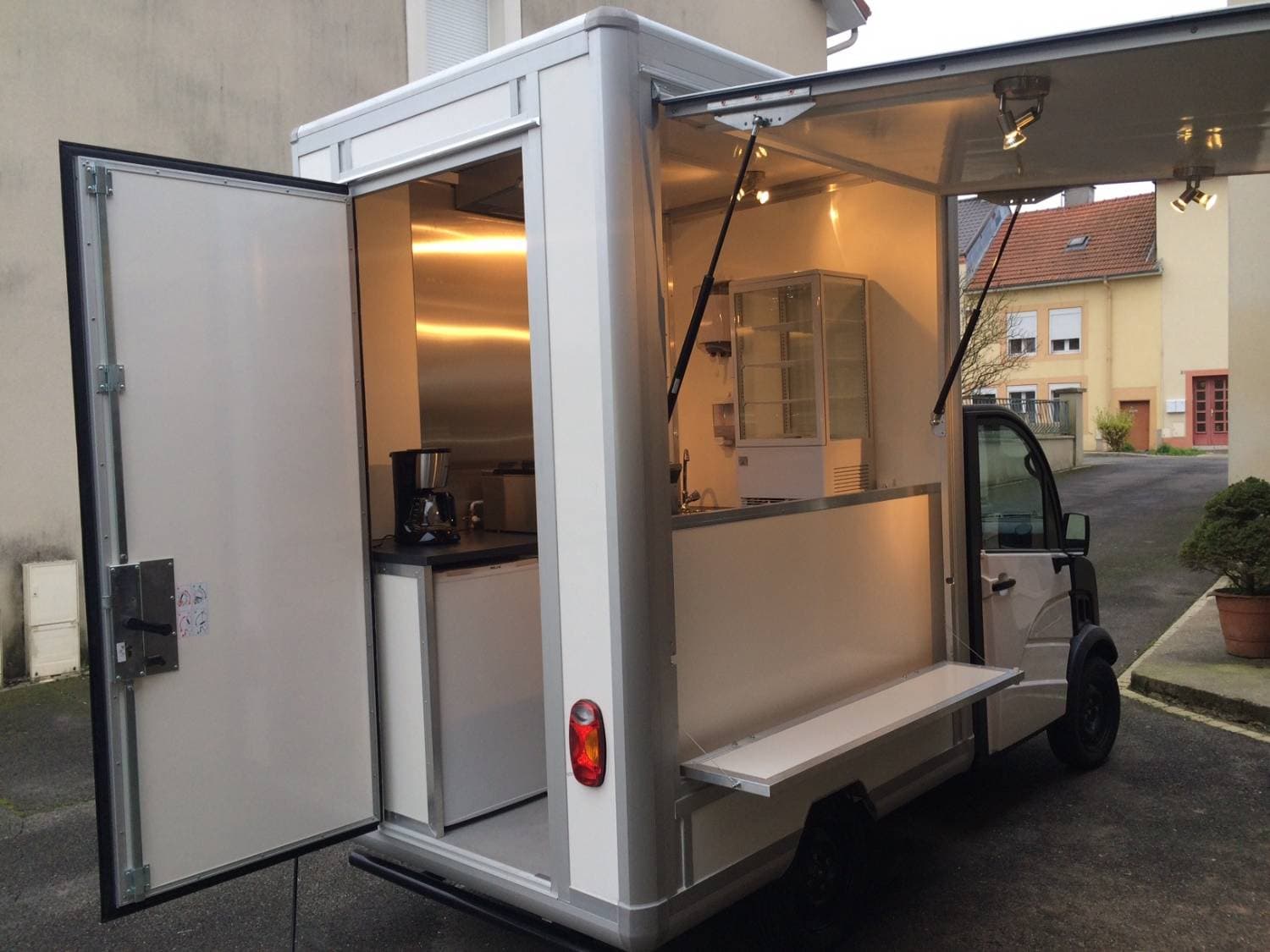 Vue arrière de l'Aixam Mega ouvert montrant cuisine équipée avec cafetière, vitrine et comptoir de service