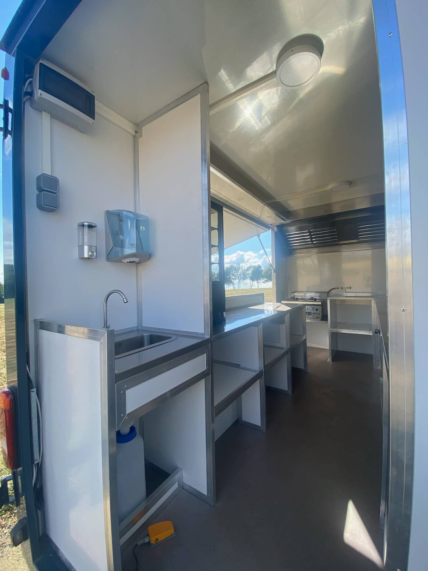 Arrière food truck barbecue ouvert avec évier, distributeurs hygiène, plaque de cuisson et vue sur campagne