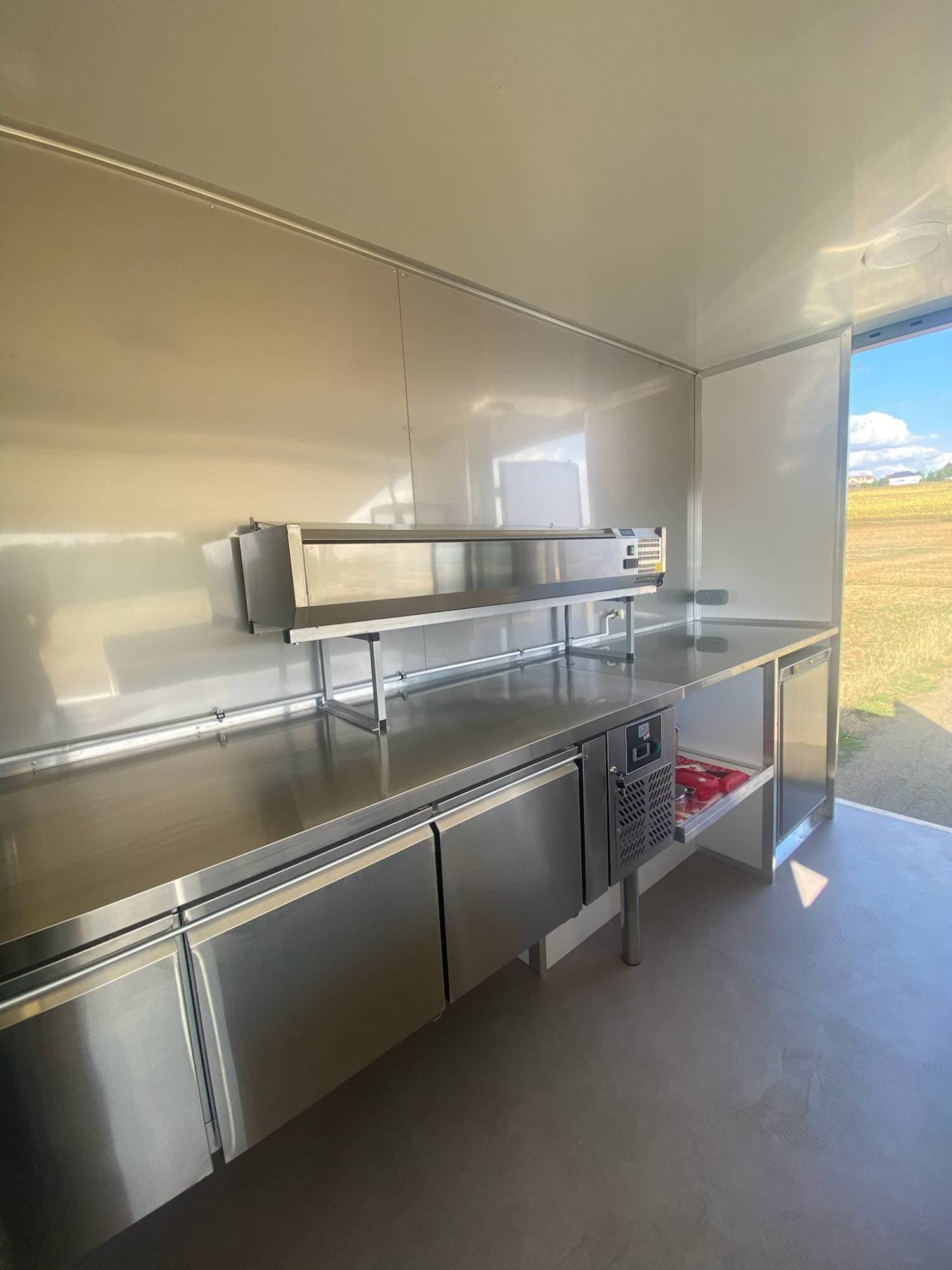 Zone de service food truck BBQ avec long comptoir réfrigéré inox, étagère supérieure et ouverture latérale