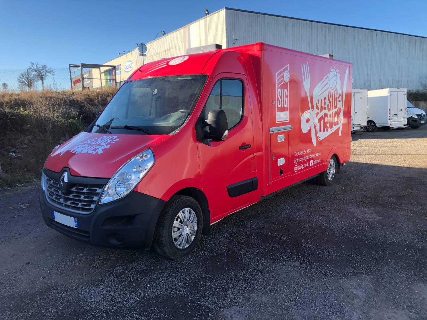 Food truck Le SIG Truck rouge Renault Master avec covering complet stationné devant un entrepôt