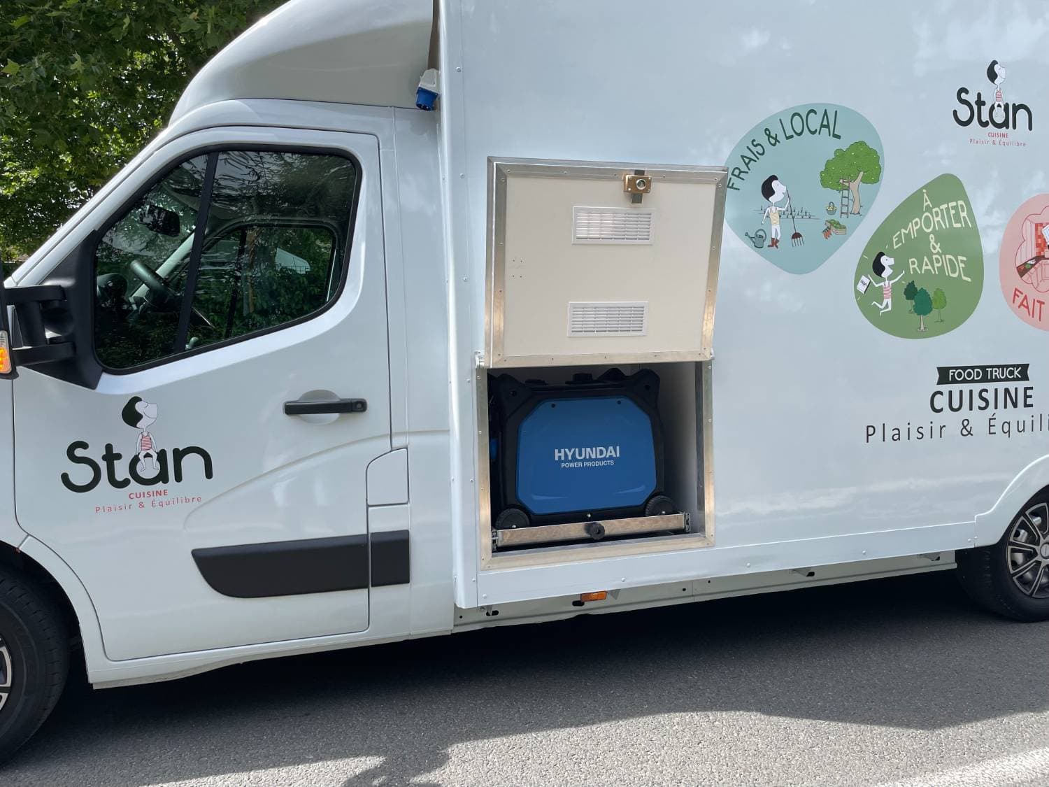 Détail latéral camion traiteur Stan blanc avec compartiment générateur Hyundai ouvert et logos Frais et Local