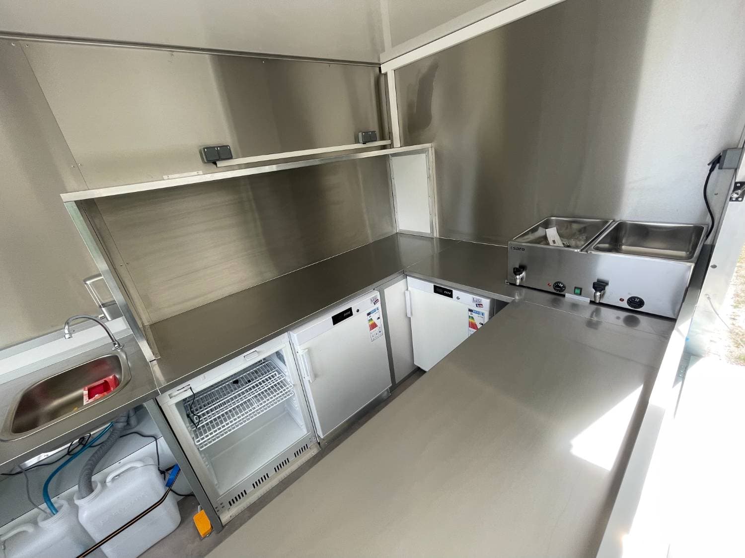Arrière cuisine camion traiteur Stan avec évier, réfrigérateurs sous comptoir, bain-marie Saro et plan de travail inox