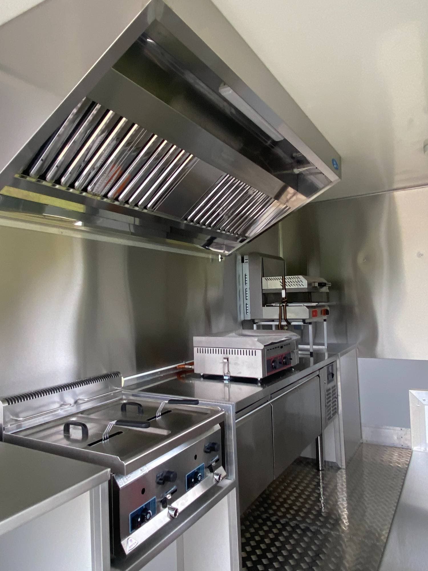 Zone cuisson food truck burger avec friteuse, plancha, hotte aspirante professionnelle et plans de travail inox