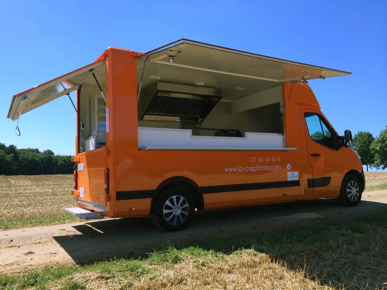Food truck orange La Crépitante ouvert avec volets relevés montrant la cuisine, stationné en campagne