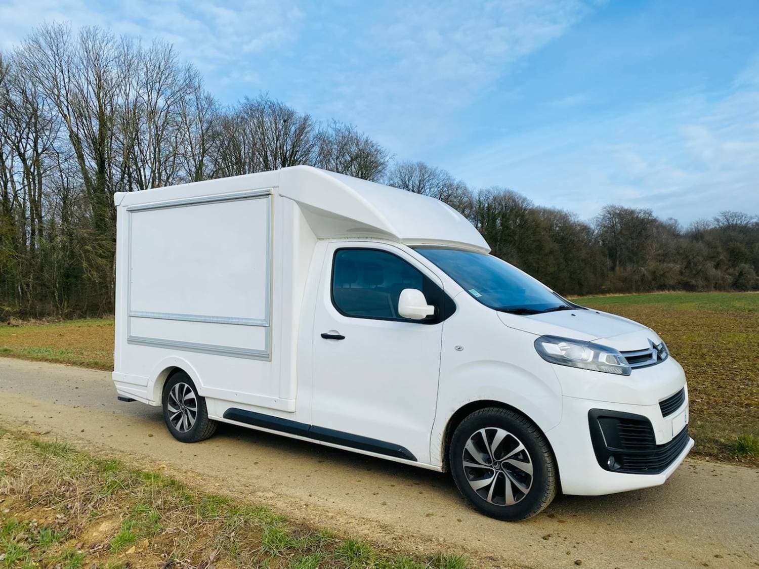 Citroën Jumpy blanc aménagé en food truck avec cellule de vente fermée — vue latérale sur chemin de campagne