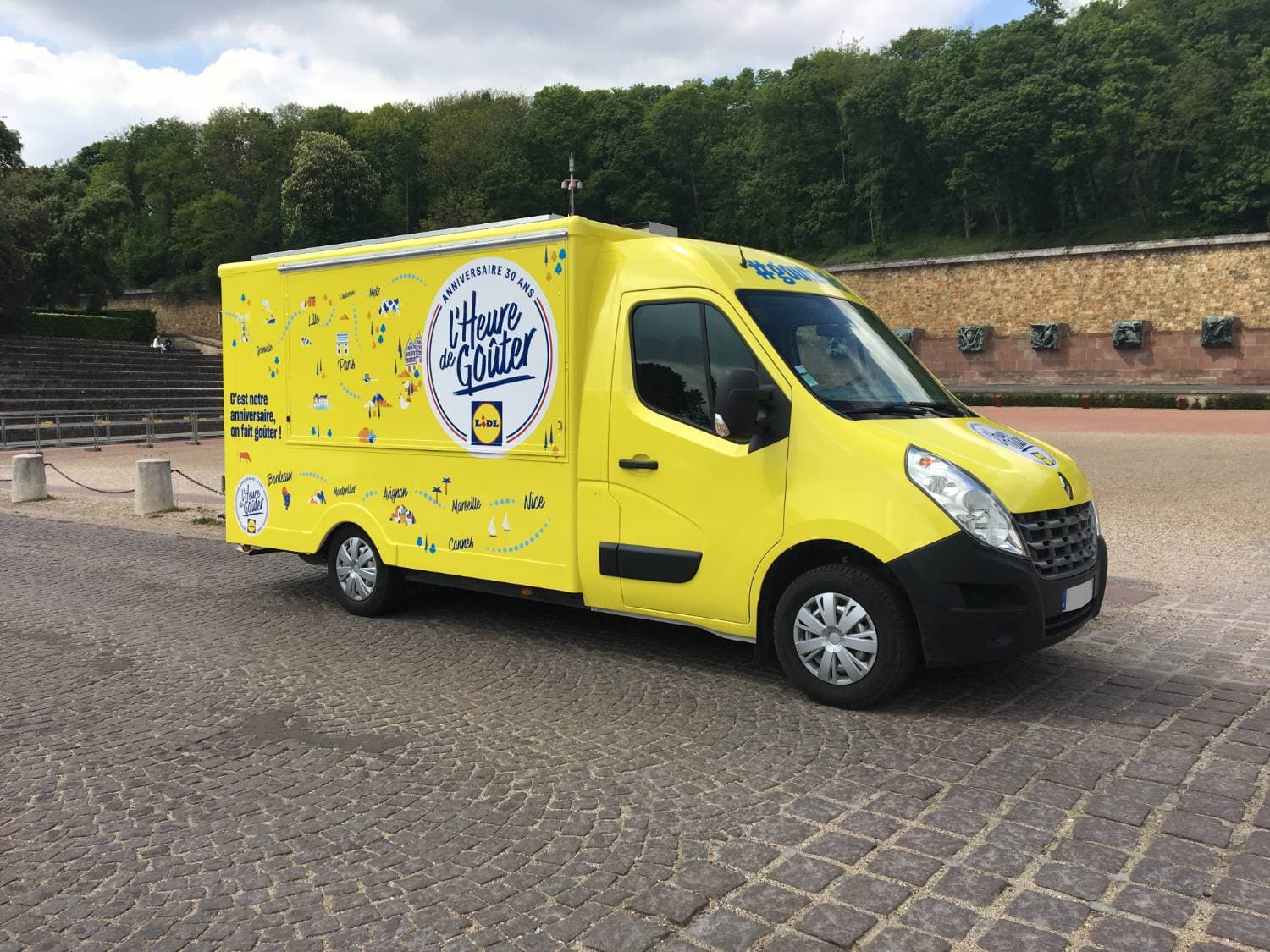 Food truck Lidl L'Heure de Goûter jaune vue trois quarts avant avec carte de France du tour sur place pavée