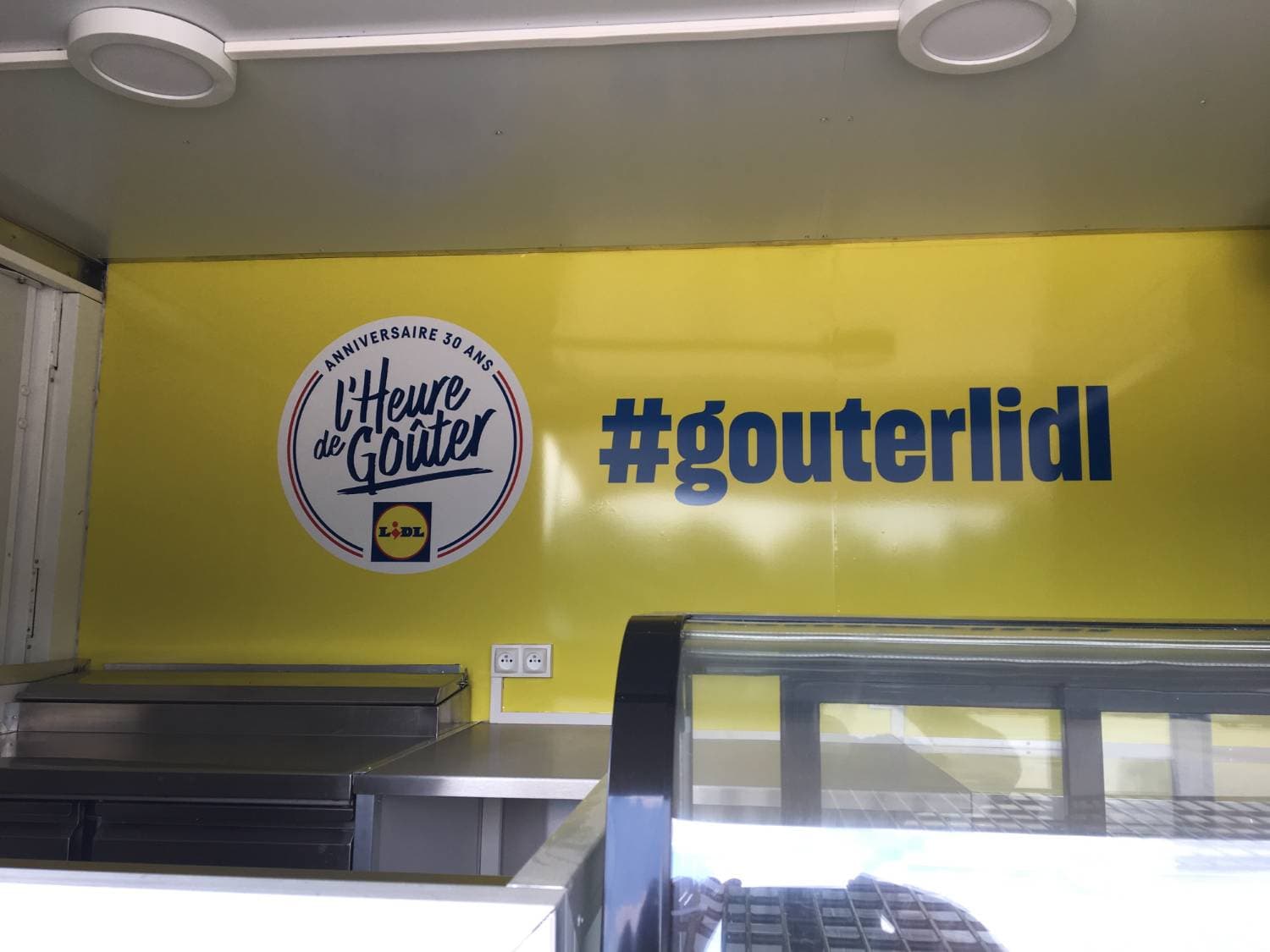 Intérieur du food truck Lidl avec logo L'Heure de Goûter hashtag #gouterlidl et vitrine réfrigérée