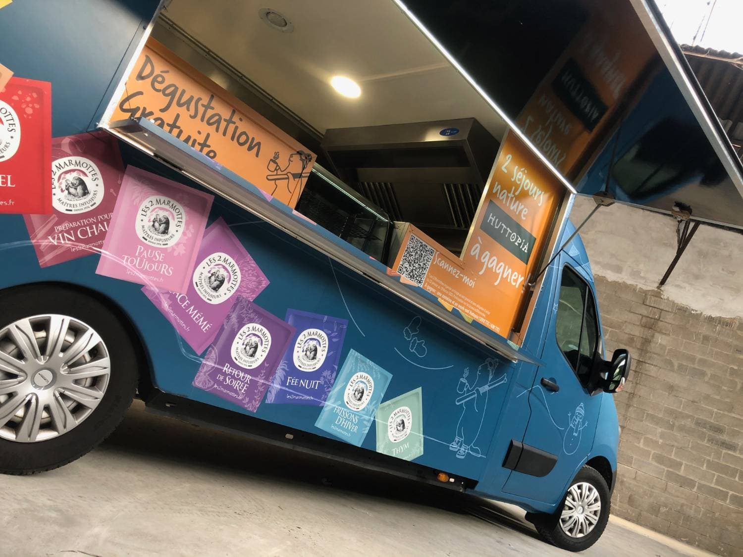 Détail du food truck Les 2 Marmottes bleu avec comptoir ouvert panneau Huttopia et sachets de thés colorés
