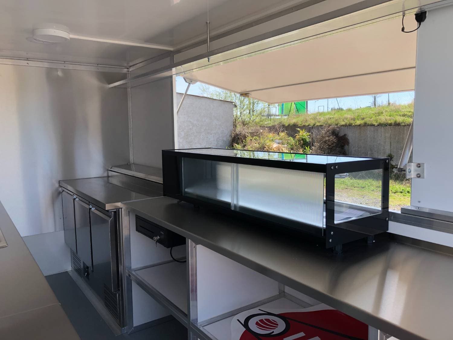 Intérieur cuisine du sushi truck Ouysabi avec vitrine à sushis noire, plan de travail inox et réfrigérateur