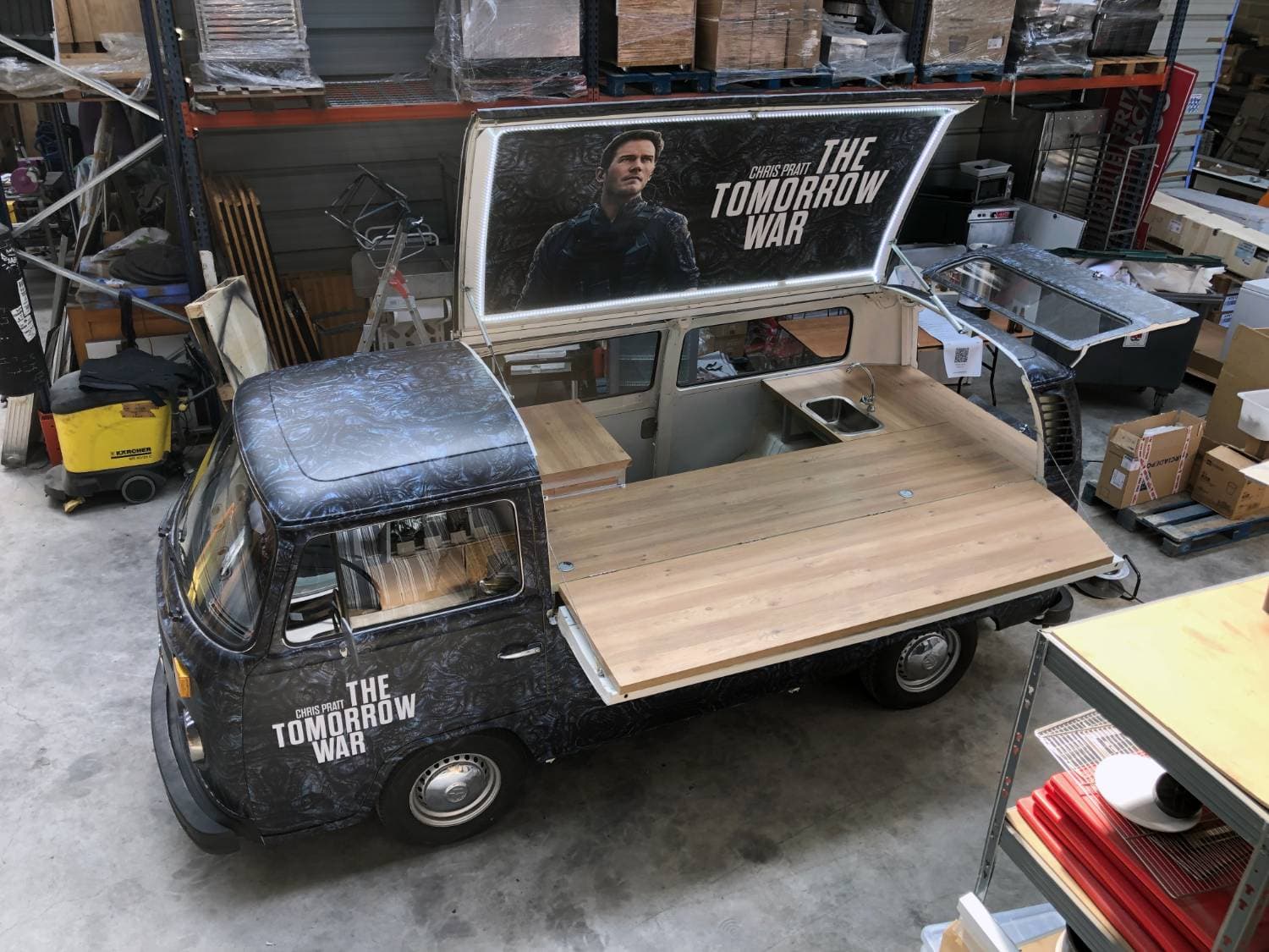 Combi VW pick-up avec total covering The Tomorrow War vu en plongée dans l'atelier — comptoir en bois et panneau lumineux
