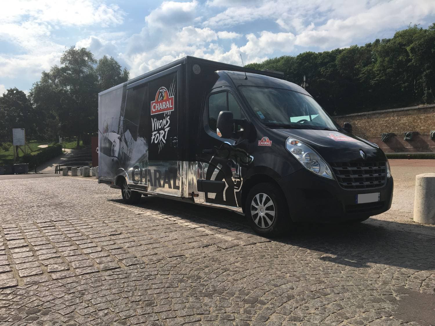 Renault Master noir avec total covering Charal Vivons Fort stationné sur pavés, vue trois-quarts avant