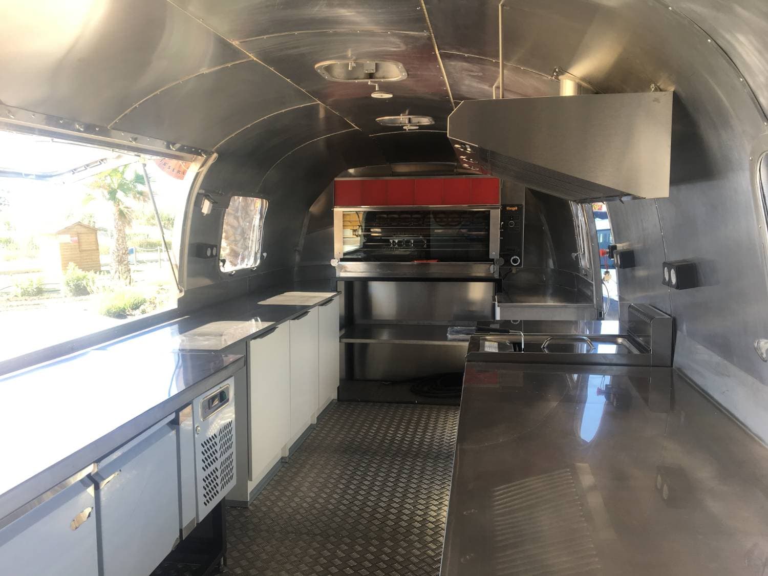 Intérieur Airstream — cuisine inox complète avec rôtissoire, plans de travail et sol damier aluminium