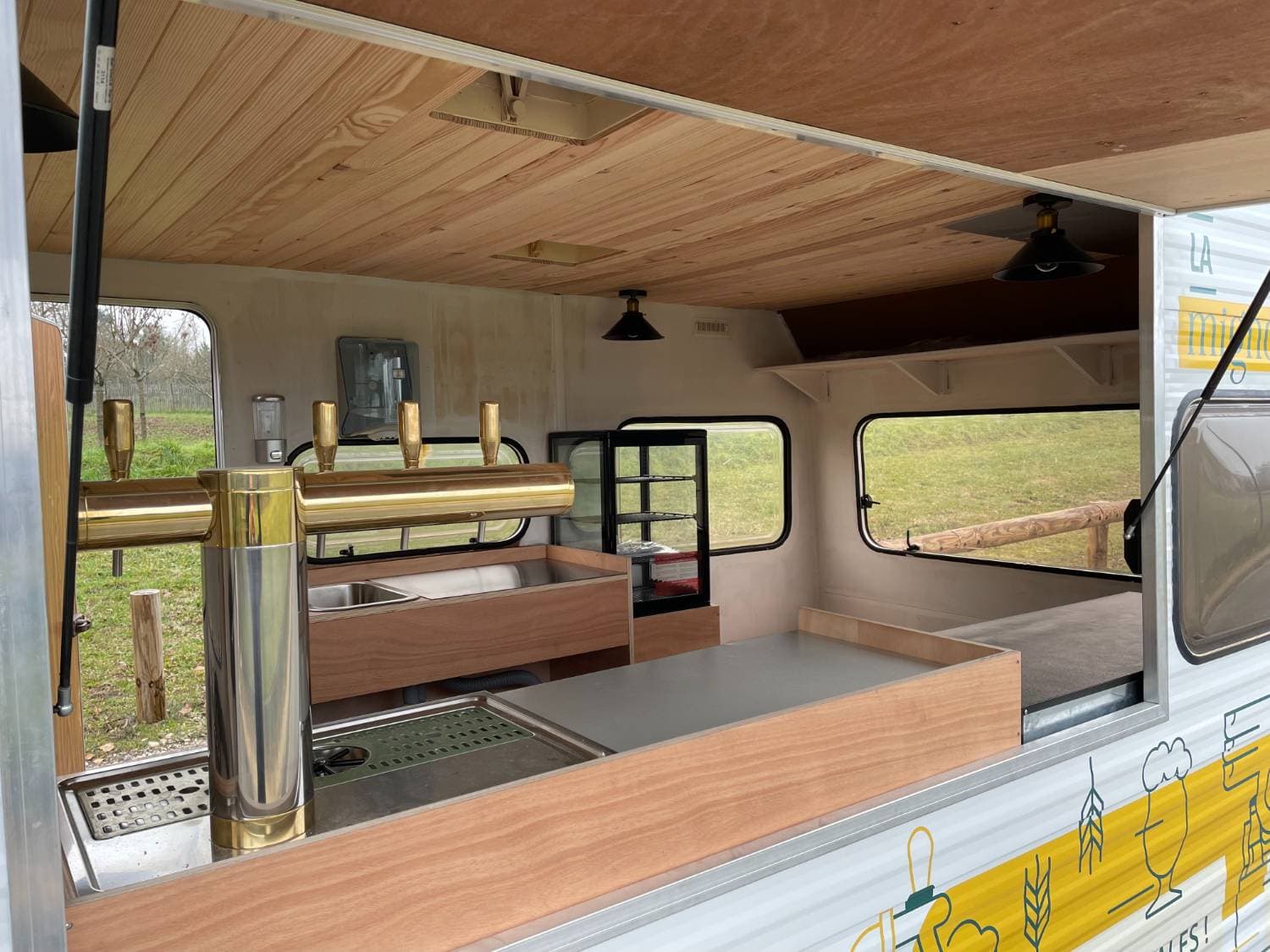 Vue intérieure du comptoir bar La Mignonnerie — robinets à bière dorés, comptoir bois et suspensions industrielles