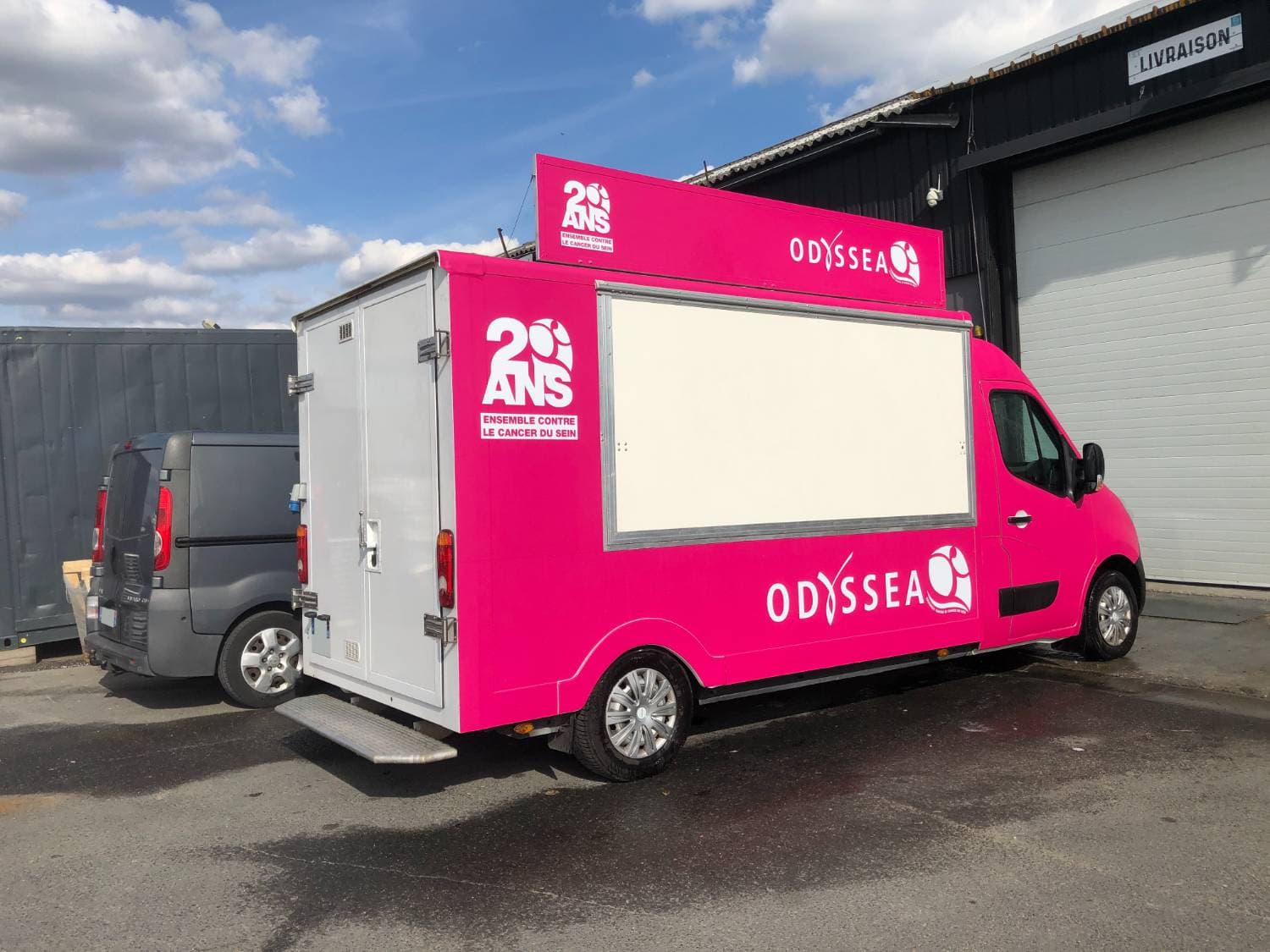 Vue arrière du Renault Master Odyssea avec hayon et covering rose devant un entrepôt