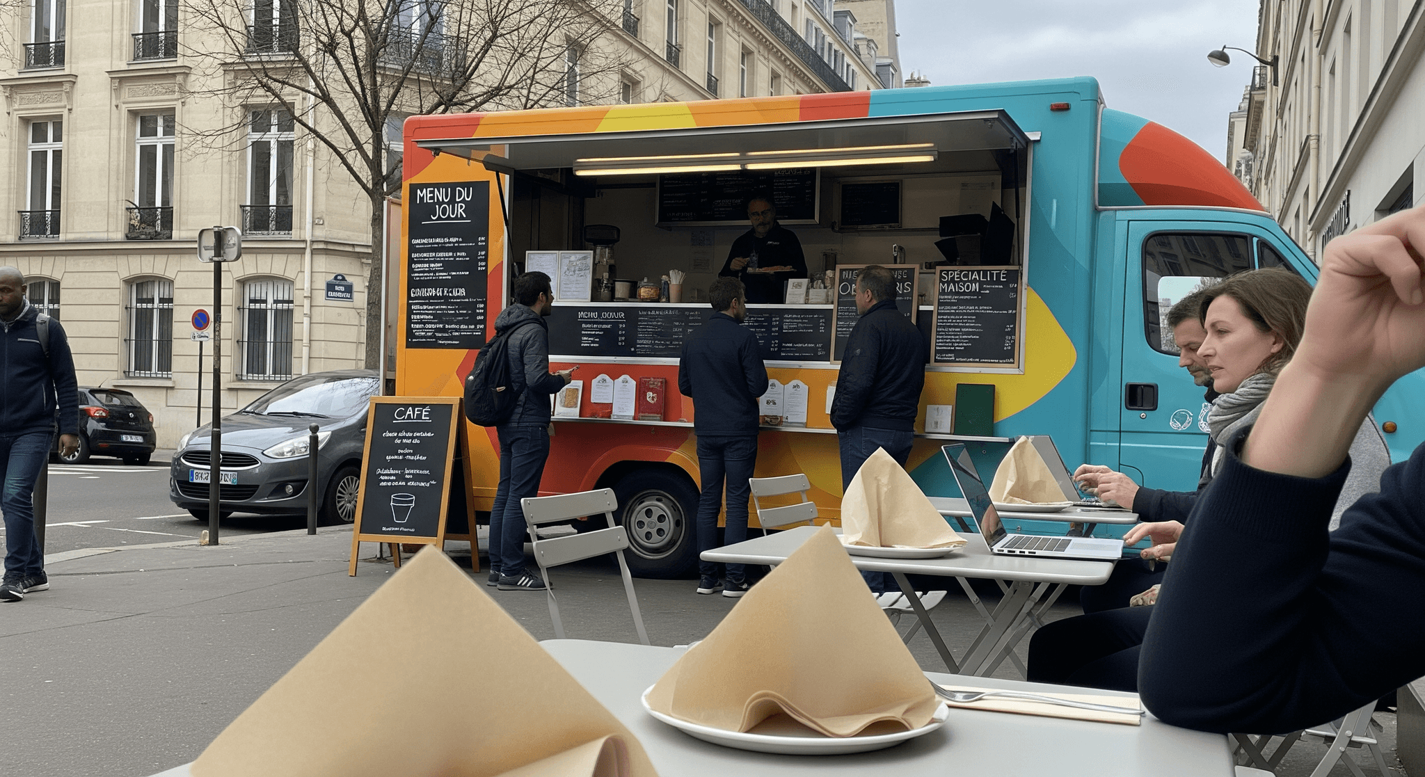 Food truck MCR aux couleurs vives (turquoise, orange, jaune) servant des clients en ville, avec terrasse et coworkers.