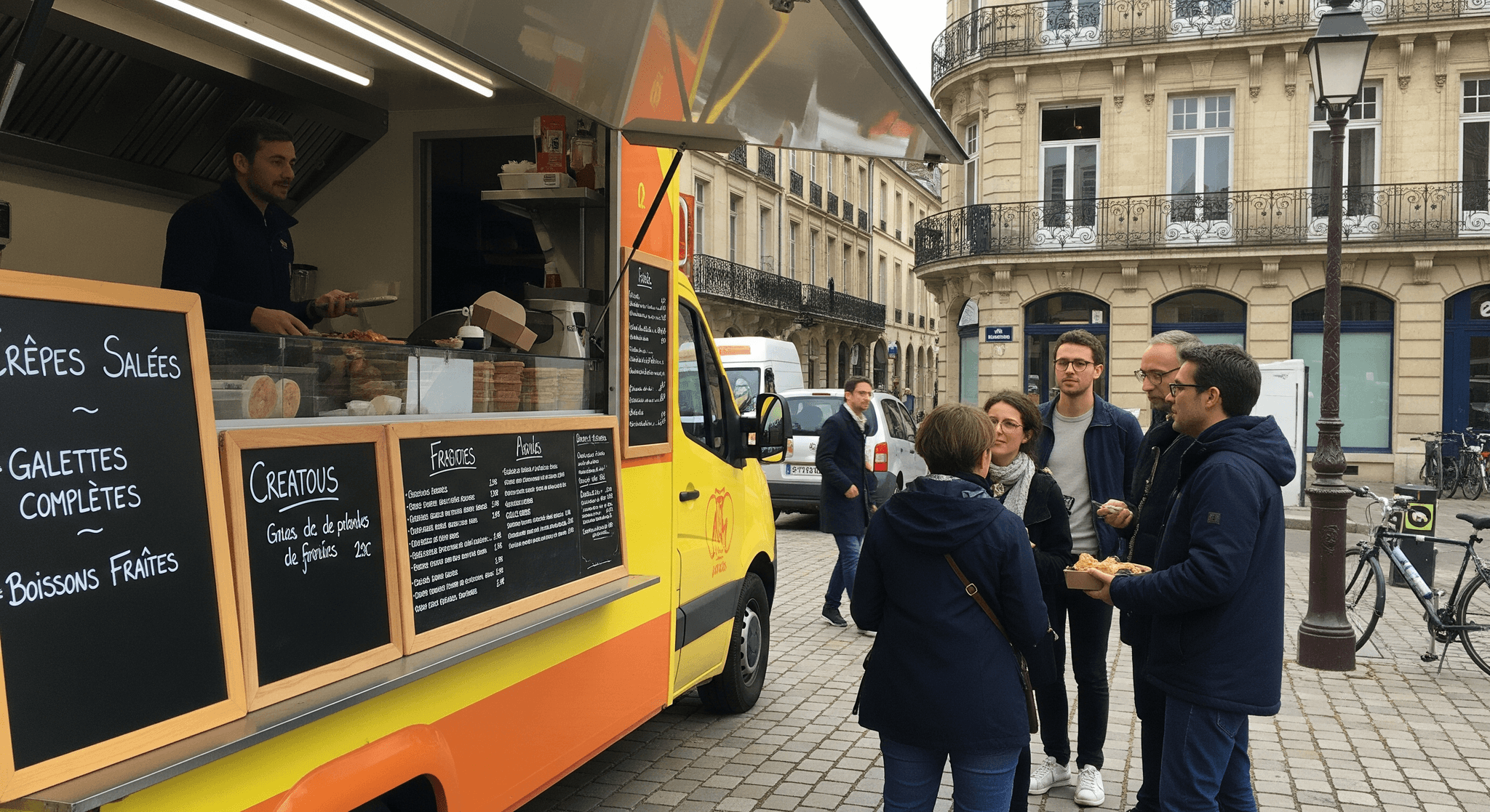 Camion food truck jaune et orange aménagé en crêperie mobile, servant crêpes et galettes à des clients en ville.