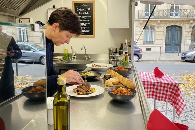 Chef dressant un plat raffiné dans un food truck équipé d'une cuisine professionnelle en inox, prêt pour la restauration mobile.