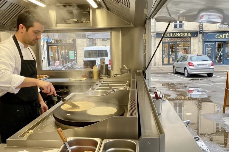 Cuisinier prépare crêpes sur double crêpière professionnelle dans remorque food truck MCR, cuisine mobile inox.
