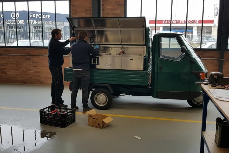 Techniciens MCR aménagent un triporteur Piaggio vert en food truck, installant l'équipement de cuisine professionnel en inox.