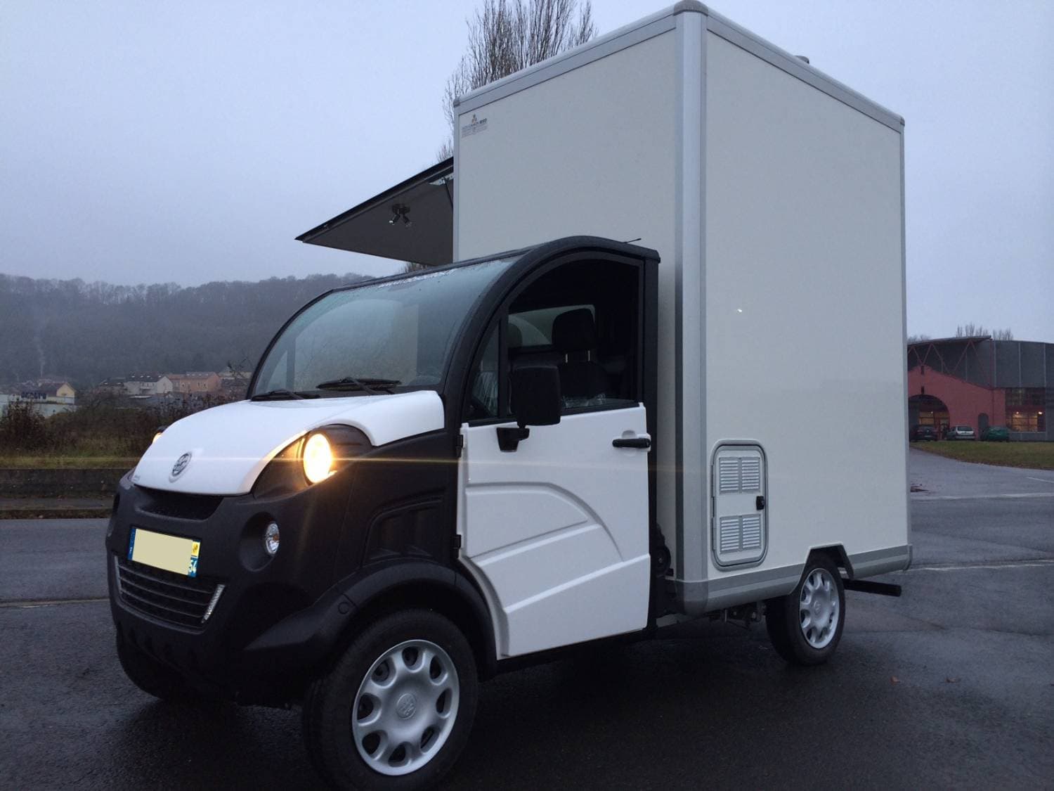 Aixam Mega blanc et noir avec cellule aménagée, vue trois-quarts avant sur parking par temps couvert