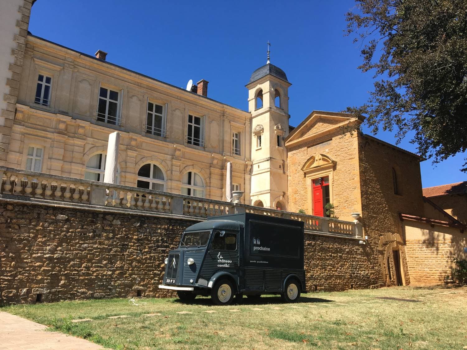 Citroën Type H gris foncé Château Contiki garé devant un château en pierre avec clocher sous ciel bleu