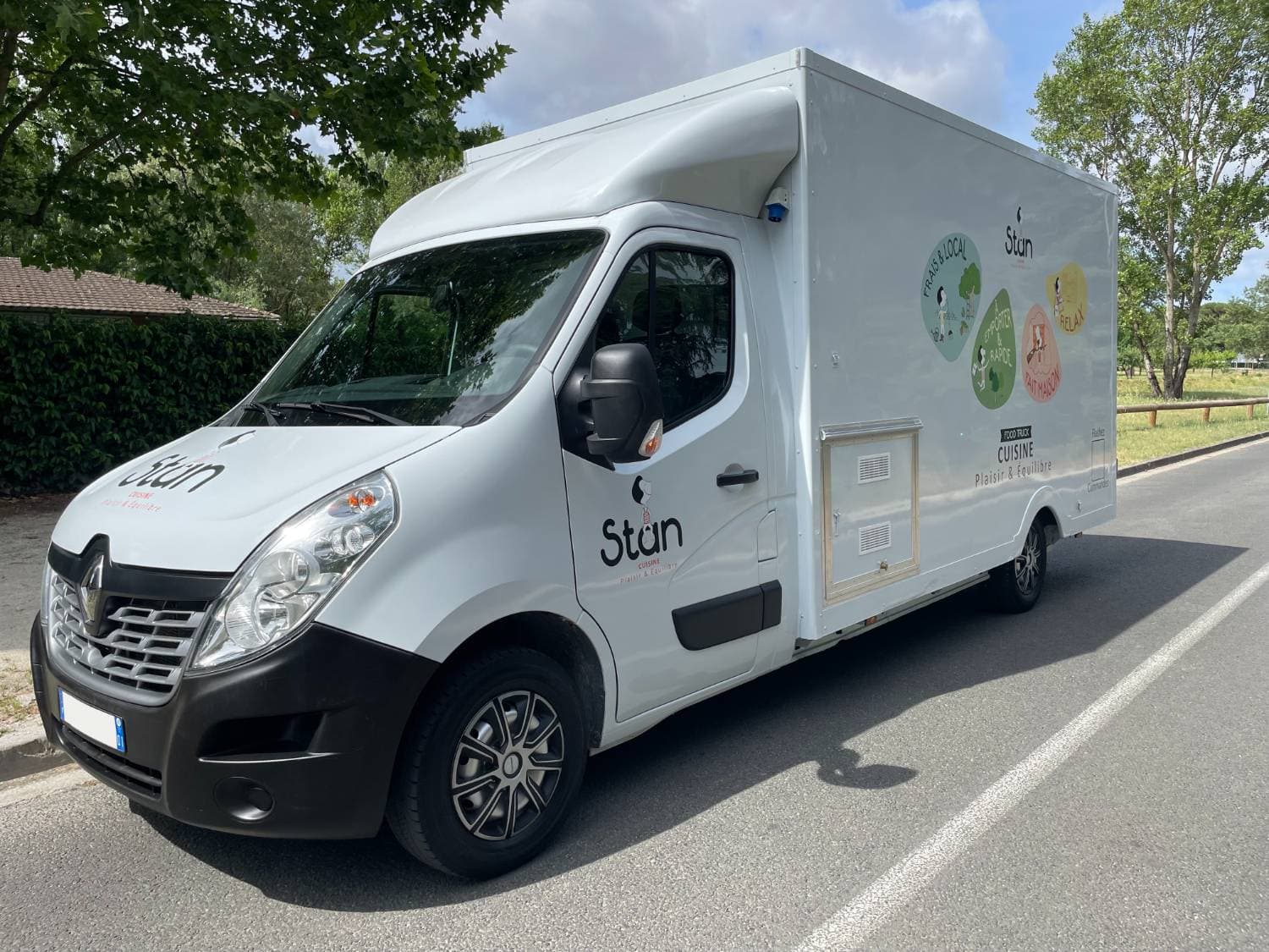 Camion traiteur Stan blanc Renault Master avec covering coloré Cuisine Plaisir et Équilibre stationné sur route