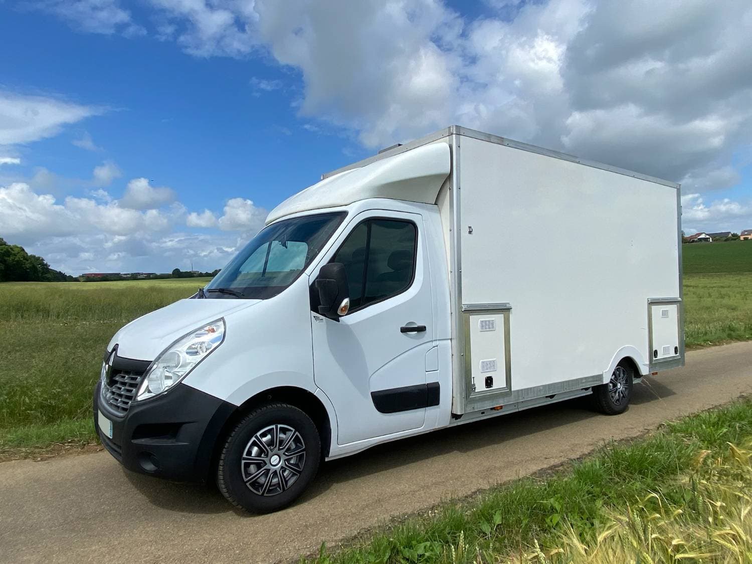 Camion traiteur blanc Renault Master fermé stationné sur chemin de campagne avec ciel nuageux