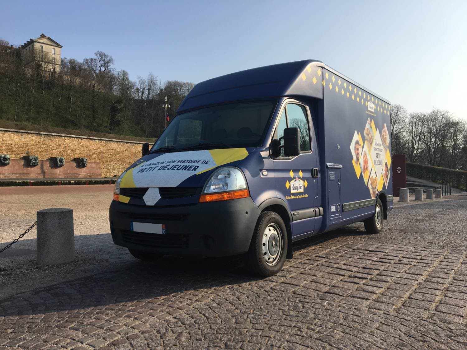 Food truck Brioche Pasquier bleu marine avec covering petit déjeuner garé sur une place pavée historique