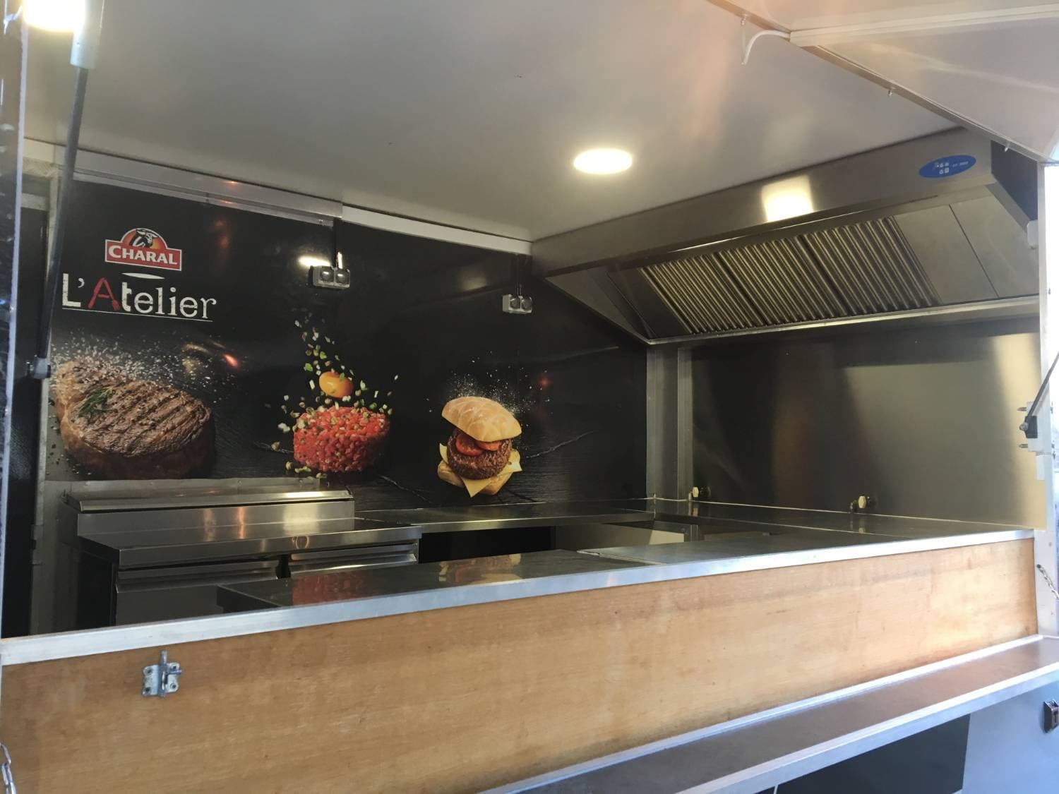 Intérieur du food truck Charal L'Atelier avec comptoir bois, plancha inox et habillage mural visuels burgers