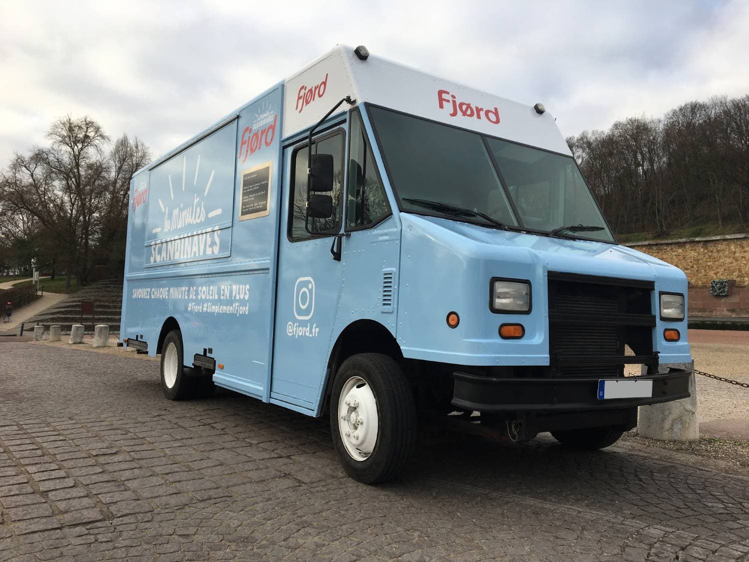 Step Van bleu ciel Fjord Les Minutes Scandinaves vue trois-quarts avant sur esplanade pavée