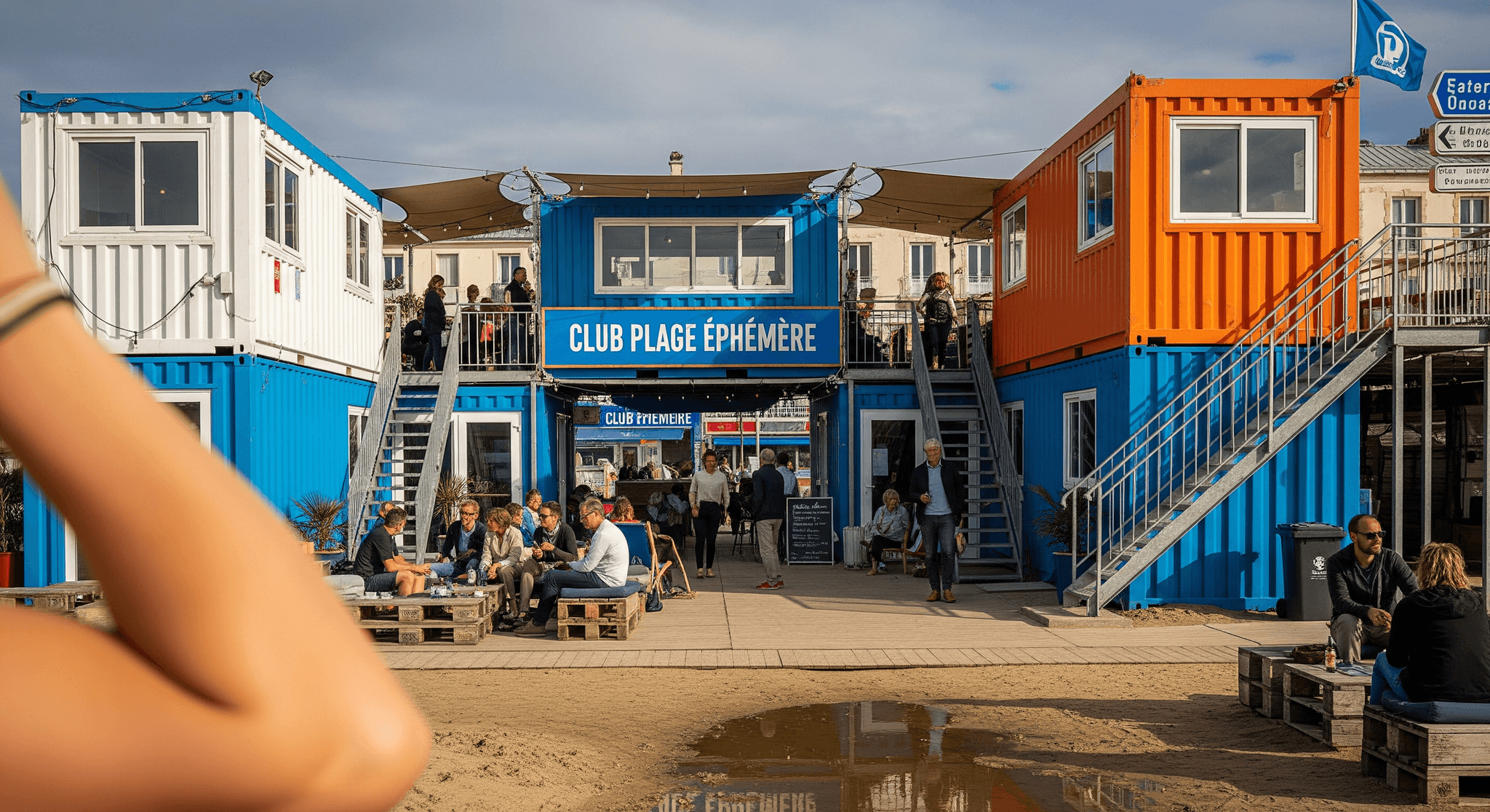 Club de plage éphémère MCR : containers aménagés modulaires bleu, blanc, orange, avec terrasses et escaliers.