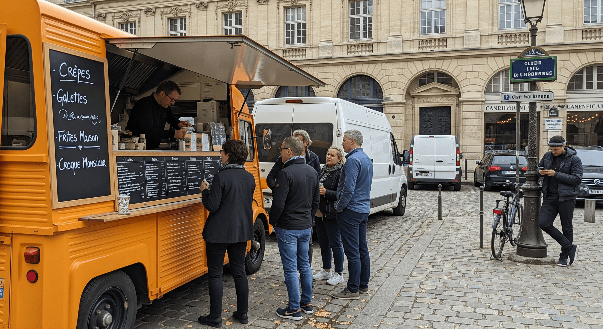 Food truck orange rétro aménagé en crêperie mobile servant crêpes, galettes et frites à des clients sur une rue pavée.