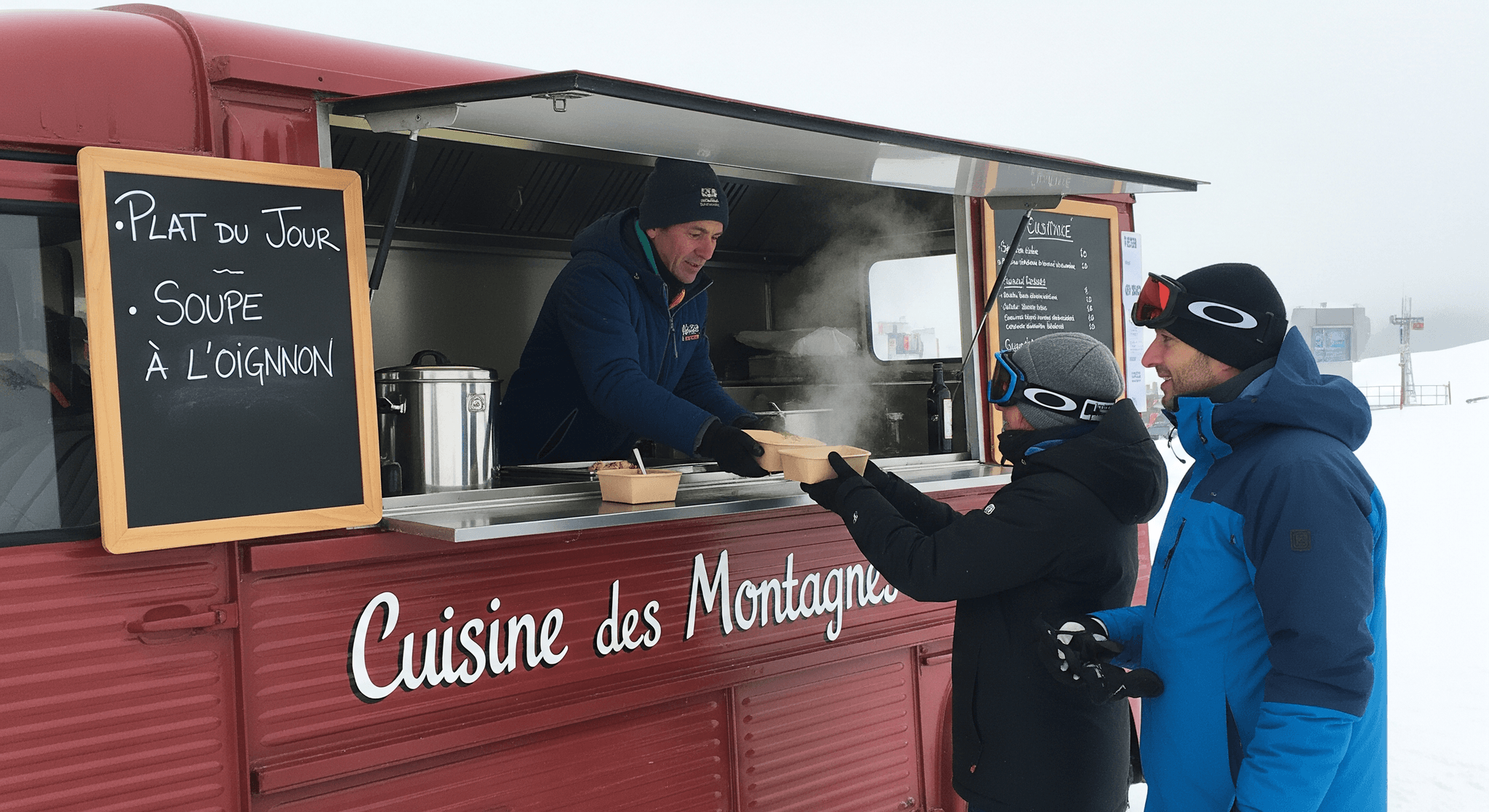Remorque food truck rouge "Cuisine des Montagnes" sert une soupe fumante à des skieurs en station enneigée.